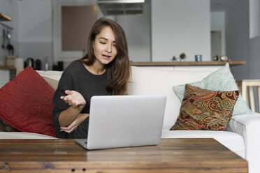Young woman sitting on her couch, chatting on her laptop - ERRF00615