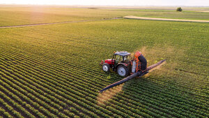 Serbia, Vojvodina, Aerial view of a tractor spraying soybean crops - NOF00074