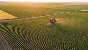 Serbia, Vojvodina, Aerial view of a tractor spraying soybean crops - NOF00075