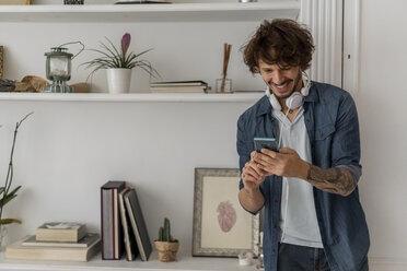 Mann arbeitet im Stehen in einem Coworking Space, benutzt ein Smartphone, hat Kopfhörer um den Hals - AFVF02226