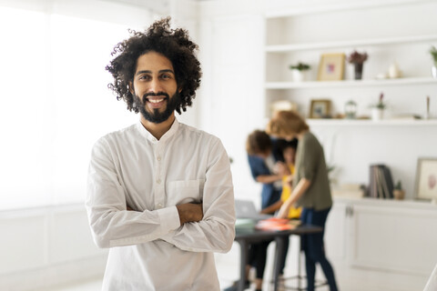 Porträt eines jungen Mannes mit Kollegen, die in einem Coworking Space arbeiten, lizenzfreies Stockfoto