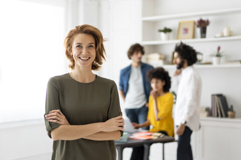 Porträt einer jungen Frau mit Kollegen, die in einem Coworking Space arbeiten, lizenzfreies Stockfoto