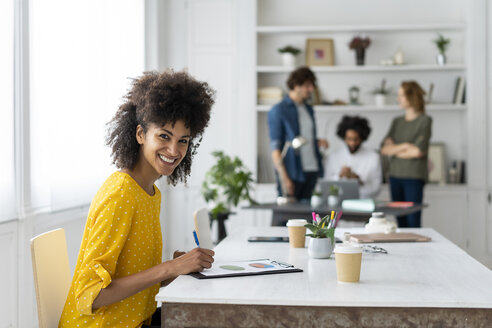 Woman woking in cowrking space, with colleagues discussing in background - AFVF02271