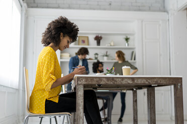 Frau bei der Arbeit im Coworking Space, im Hintergrund diskutieren Kollegen - AFVF02273