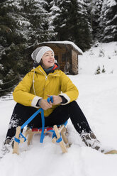 Austria, Tyrol, Thurn, content mature woman sitting on sledge in the snow looking at distance - PSIF00212