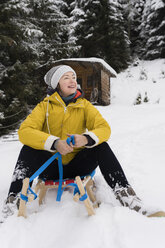 Österreich, Tirol, Thurn, zufriedene reife Frau sitzt auf Schlitten im Schnee und schaut in die Ferne - PSIF00212