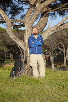 Wanderer mit Rucksack während einer Wanderung, an einen Baum gelehnt, Sonnenbad nehmend - KBF00400