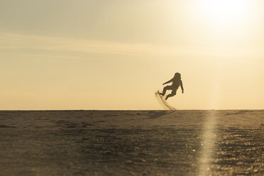 Mann mit Rucksack springt am Strand im Abendlicht - KBF00405