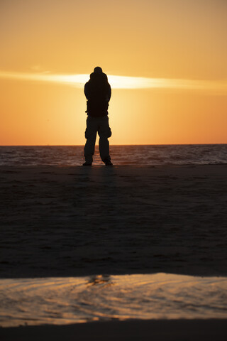 Mann mit Rucksack am Strand im Abendlicht, lizenzfreies Stockfoto