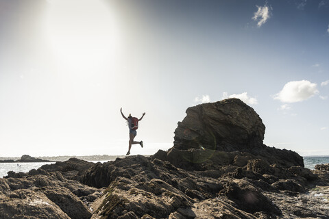 Junge Frau rennt und springt an einem felsigen Strand, lizenzfreies Stockfoto