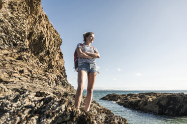 Junge Frau wandert an einem felsigen Strand und betrachtet die Aussicht - UUF16467