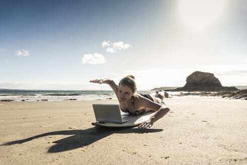 Young woman lying on surfboard, using laptop - UUF16478