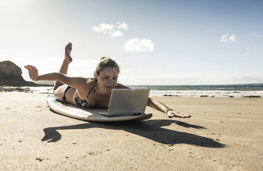 Junge Frau liegt auf einem Surfbrett und benutzt einen Laptop - UUF16479