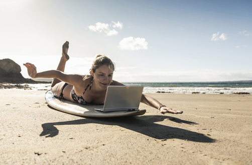 Young woman lying on surfboard, using laptop - UUF16479