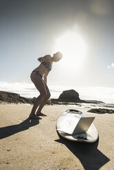 Junge Frau steht am Surfbrett und benutzt einen Laptop - UUF16480