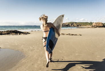 Young woman running on the beach, carrying surfboard - UUF16487