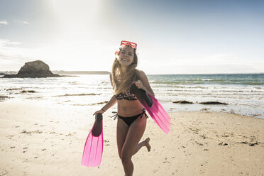 Happy young woman with snorkelling equipment, running on the beach - UUF16499