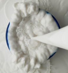 Milk being poured to overflow into bowl - CUF46972