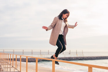 Frau springt von Geländer am Strand - CUF47080