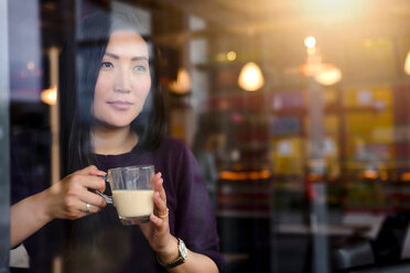 Mittlere erwachsene Frau mit Kaffee, die vom Fensterplatz eines Cafés hinausschaut - CUF47129