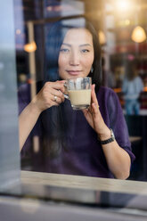 Mittlere erwachsene Frau mit Kaffee, die vom Fensterplatz eines Cafés hinausschaut, Porträt - CUF47130