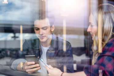 Young students looking at smartphones in cafe window seat, view through window - CUF47133