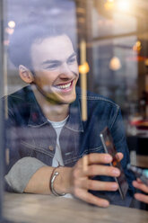 Male student showing smartphone in cafe window seat, view through window - CUF47134