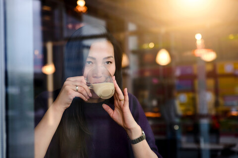 Mittlere erwachsene Frau trinkt Kaffee in Café Fensterplatz, lizenzfreies Stockfoto