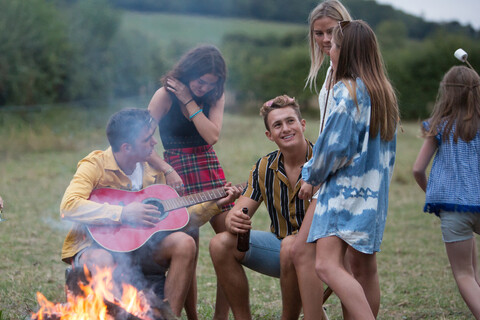 Junger Mann spielt Gitarre bei Lagerfeuerparty im Park, lizenzfreies Stockfoto