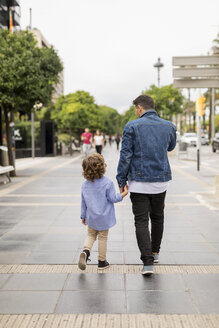 Rückansicht von Vater und Sohn, die Hand in Hand in der Stadt spazieren gehen - MAUF02288