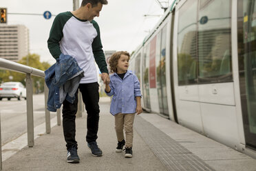 Lächelnder Vater und Sohn gehen Hand in Hand an einer Straßenbahnhaltestelle in der Stadt - MAUF02291