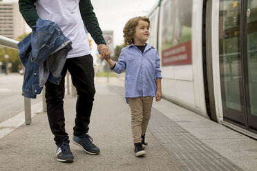 Father and son walking hand in hand at tram stop in the city - MAUF02292