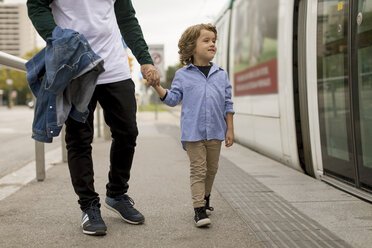 Vater und Sohn gehen Hand in Hand an einer Straßenbahnhaltestelle in der Stadt - MAUF02292