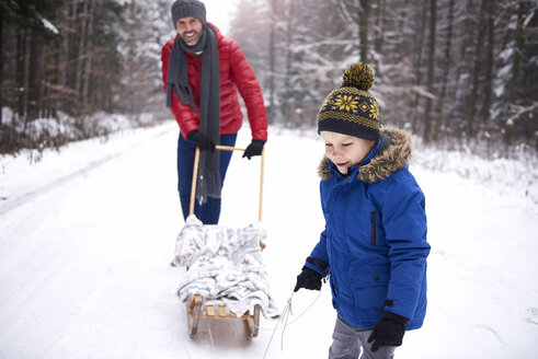 Zufriedener kleiner Junge und sein Vater mit Schlitten im Winterwald - ABIF01128