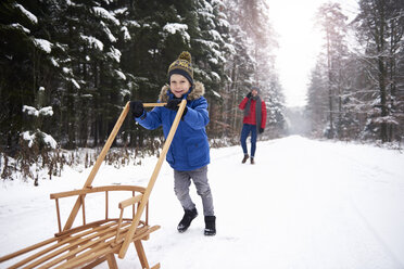 Little boy pushing sledge in winter forest while his father watching him from background - ABIF01130