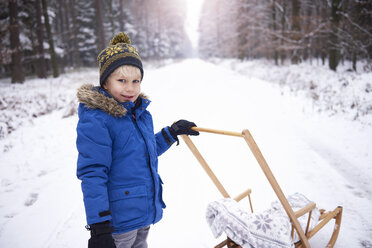 Portrait of smiling little boy with sledge in winter forest - ABIF01139