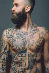 Portrait of young man with beard, bare chest covered in tattoos - CUF47207