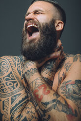 Portrait of young man with beard, covered in tattoos, hands around throat, screaming - CUF47209