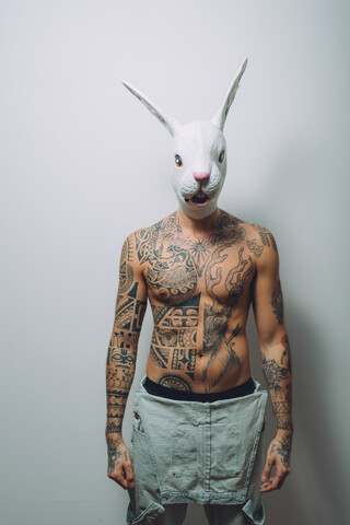 Portrait of young man with wearing rabbit mask, bare chest covered in tattoos stock photo