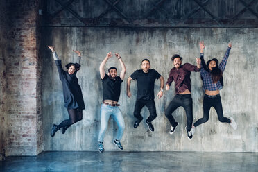 Kollegen beim Springen posieren für ein Gruppenfoto vor einer Betonwand - CUF47225