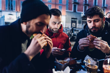 Freunde genießen einen Burger in einem Straßencafé, Mailand, Italien - CUF47245