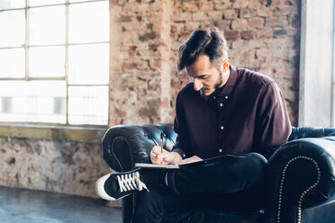 Man in armchair writing notes - CUF47255