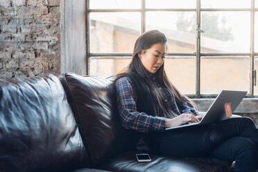 Frau auf Sofa am Fenster mit Laptop - CUF47292