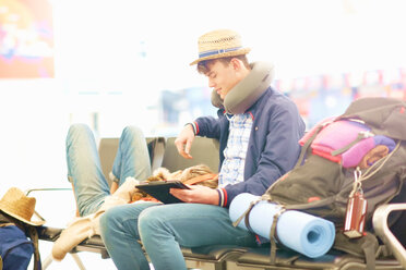 Young couple in departure lounge at airport, woman resting head on man's legs, man using digital tablet - CUF47305