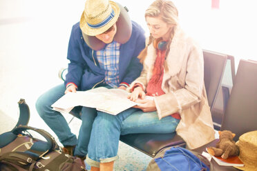 Young couple sitting in airport departure lounge, looking at map, planning trip - CUF47307