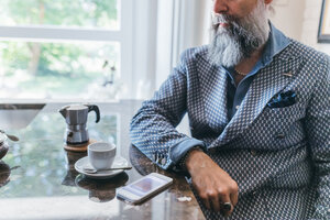 Mann benutzt Mobiltelefon bei Kaffee in der Küche - CUF47348