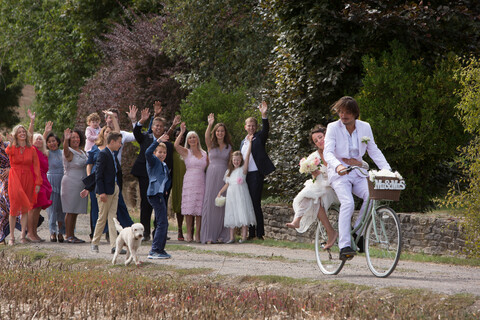 Wedding guests waving off newlyweds on bicycles stock photo