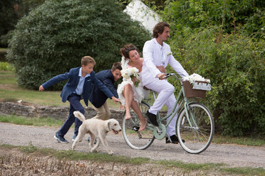 Junge Hochzeitsgäste, die dem Brautpaar auf Fahrrädern hinterherfahren - CUF47461