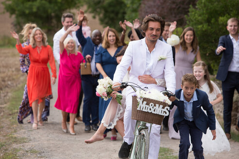 Hochzeitsgäste winken den frisch Vermählten auf Fahrrädern zu - CUF47462