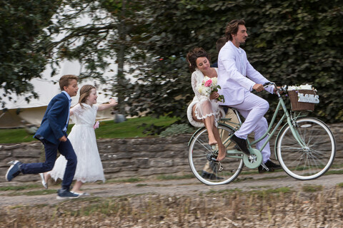 Young wedding guests running after newlyweds on bicycles stock photo